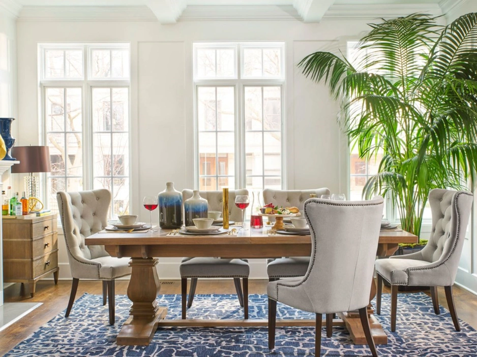 Stylish dining room with large windows, elegant chairs, a wooden table, decorative vases, and lush indoor plants.